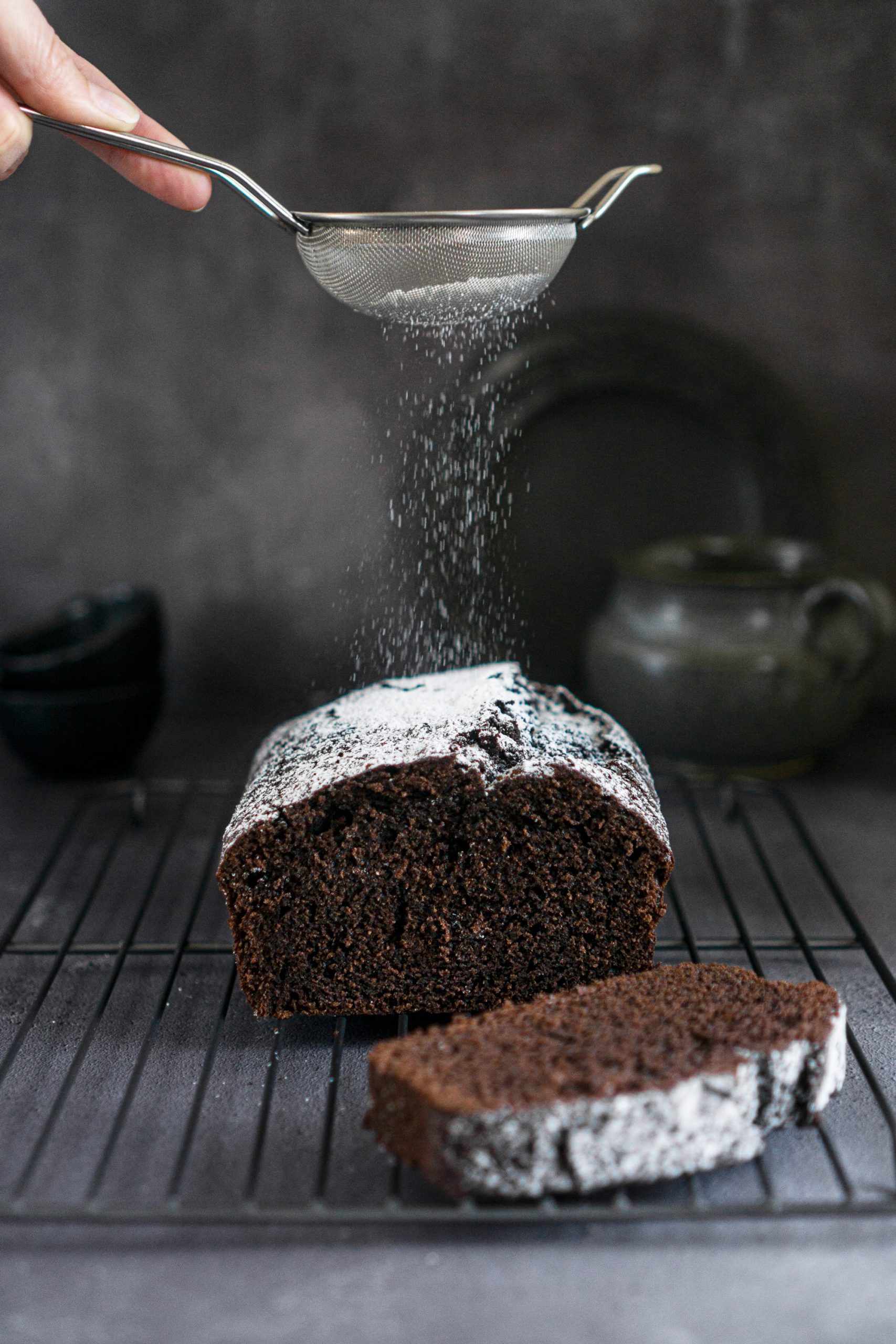 Moist chocolate loaf cake being dusted with powdered sugar