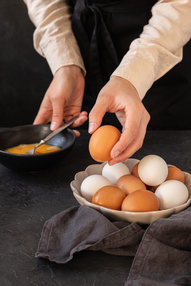 A hand of a female taking a raw egg from the bowl