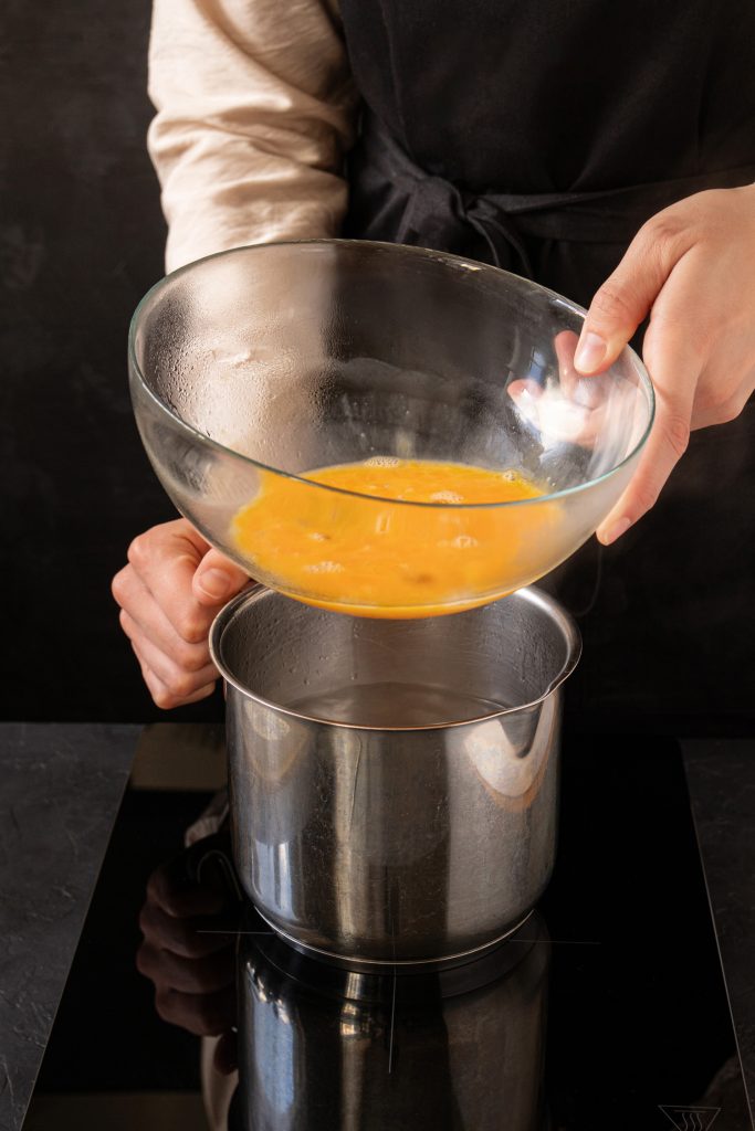 Woman putting a bowl with raw liquid eggs on top of a steaming water pasteurize them